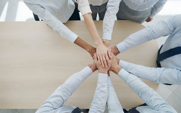 Diverse hands joining in unity over a wooden desk during a collaborative business meeting