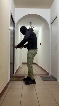 Masked burglar breaking into apartment door in residential building hallway - home burglary, 4K resolution crime concept