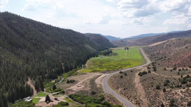 Aerial of Wolf Creek highway through mountain valley in Duchesne County Utah featuring dense coniferous forest and agricultural field and meadow along Duchesne River