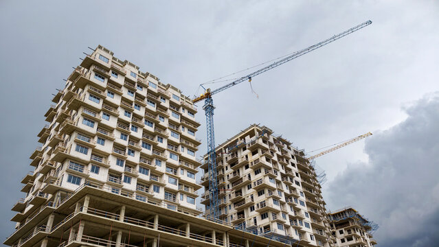 Modern residential buildings under construction with tower cranes shaping the urban landscape, symbolizing growth, development, and future housing projects against a cloudy sky