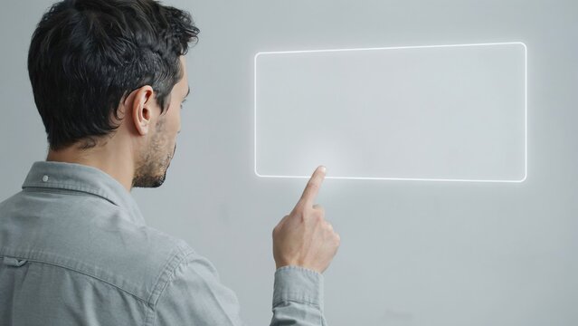 Man in a grey shirt touching a glowing rectangular holographic interface on a wall