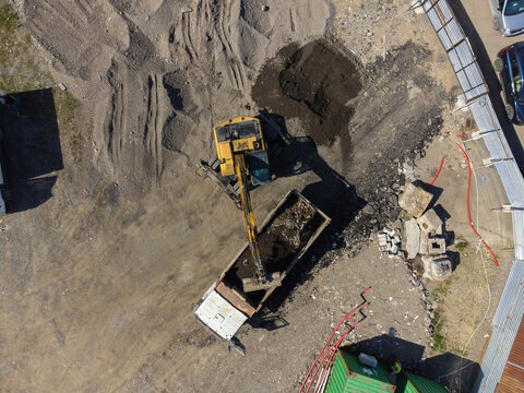Heavy machinery at work on a large construction site, with an excavator operating its arm to load soil into a waiting dump truck from an aerial perspective