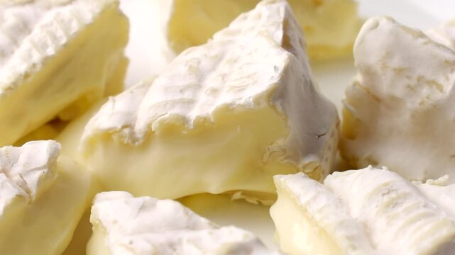 Creamy brie or camembert cheese wheel cut into wedges, soft white rind revealing gooey paleyellow interior circle rotation close up