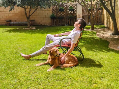 Young man relaxing with golden retriever in sunny garden