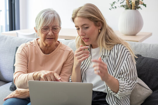 Granddaughter teaching grandmother how to use a laptop at home, bridging the generation gap and fostering digital literacy for seniors in a modern family setting