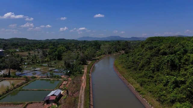 Aerial view of the irrigation canal flowing through lush green vegetation and fish ponds in Karang Intan, South Kalimantan, Indonesia.