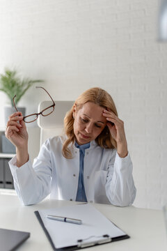 Exhausted female doctor sitting at her desk after a demanding workday. Physician burnout, healthcare stress, compassion fatigue, emotional exhaustion and medical profession