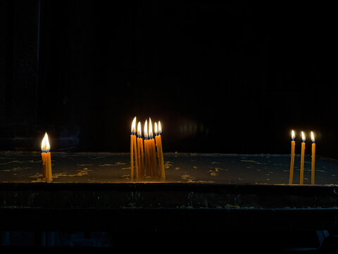 Burning candles in a church against a dark background, warm candlelight and spiritual atmosphere, traditional religious ritual