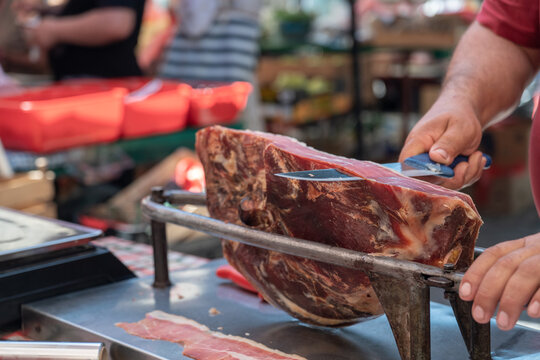 Farmer slicing traditional homemade cured ham at a local farmers market, artisanal meat preparation and authentic food tradition