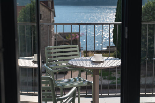 Open window leading to a balcony with a small table and cup of coffee overlooking the sea and historic old town, peaceful Mediterranean travel atmosphere