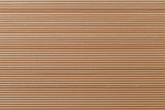 Eco cardboard surface with fine corrugated texture detail across horizontal lines creating warm natural pattern and subtle shadow contrast for packaging or background use
