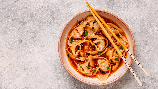 Wontons are placed in a bowl with spicy sauce.