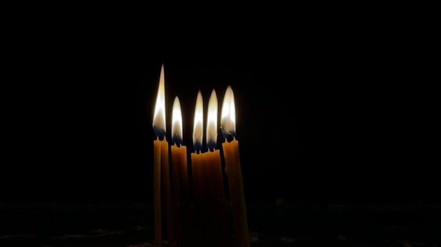Burning religious candles in a church on a dark background, warm candlelight and spiritual atmosphere