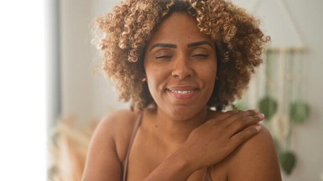 Woman smiling with teeth, hand on shoulder and bare shoulders visible in studio portrait; joy self care.