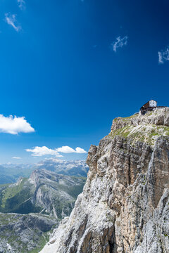 View of the Lagazuoi mountain refuge perched on a jagged rocky cliff overlooking the dramatic Dolomite peaks under a clear blue sky in Cortina d'Ampezzo, Veneto, Italy.