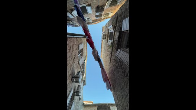 Vertical view of laundry drying on clotheslines above a narrow street in an old European city, authentic urban lifestyle and everyday life concept