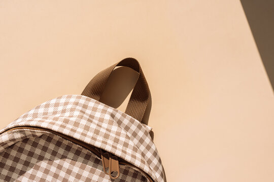 Beige checkered school backpack in warm sunlight with copy space, back to school concept.
