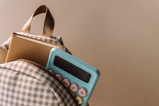 Checkered school backpack with notebook and blue calculator in warm light.