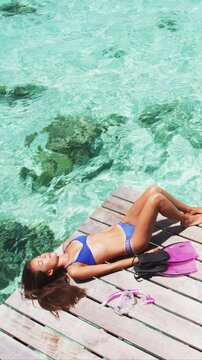 Woman relaxing on her private hotel terrace enjoying view of the ocean reefs from overwater bungalow in paradise in Tahiti, French Polynesia, Snorkeling gear. Raw vertical video of real woman.