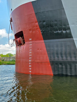 A close-up view of a Great Lakes freighter's bow features a distinctive red and black color scheme, with visible plimsoll markers indicating the highest safe depth for the ship in the water