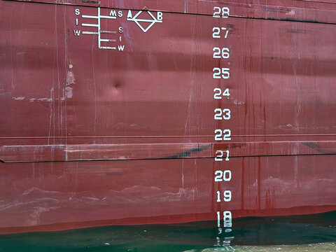 A ship's hull displays draft markings and measuring indicators that highlight its waterline and provide a sense of scale