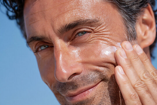 Sunlit man applying sunscreen to cheek, close up skin care routine with visible texture and smile