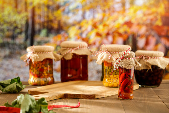Homemade preserves in glass jars on wooden table with autumn landscape background.