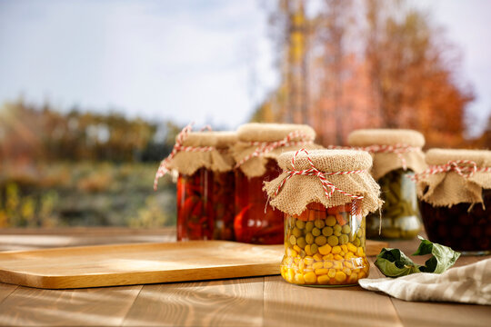 Homemade preserves in glass jars on wooden table with autumn landscape background.