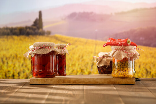 Homemade preserves in glass jars on wooden table with autumn landscape background.
