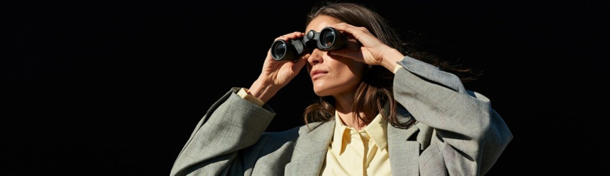 Woman looking through binoculars with dramatic dark background for observation and scouting banner background wallpaper