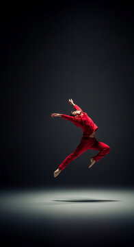 Male dancer in red attire mid-air, arms outstretched in a dynamic pose against a dark backdrop, showcasing movement, grace, and expression