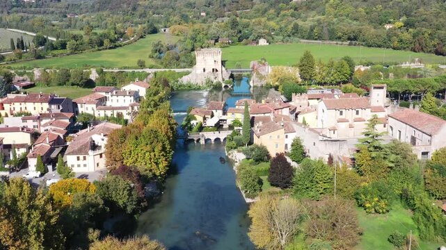 Aerial view of the historic village of Borghetto with its ancient stone buildings, water mills, and the Mincio river flowing through the lush green landscape in Borghetto, Veneto, Italy.