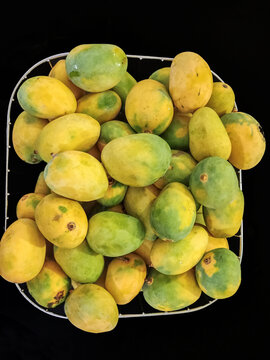 View of a wire basket filled with fresh, ripe mangoes showing a mix of yellow and green skin textures in Jahanian, Punjab, Pakistan.