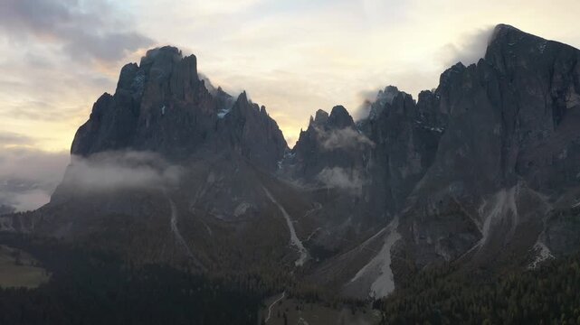 Aerial view of the majestic Langkofel Group peaks at sunset with soft clouds drifting over the rocky slopes in Santa Cristina Gherdeina, Trentino-Alto Adige, Italy.