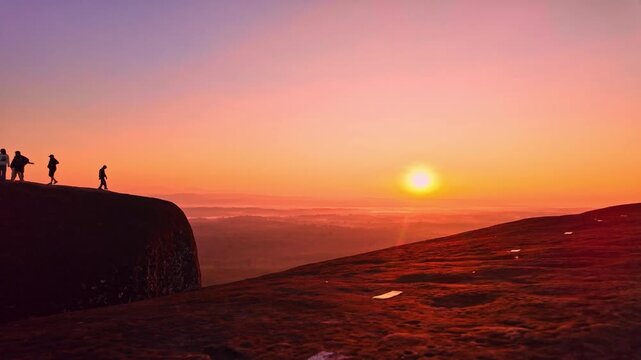 A breathtaking sunrise panorama captures tourists gathered on the massive whale shaped cliffs of Three Whale Rock, overlooking misty mountains and endless tropical wilderness.