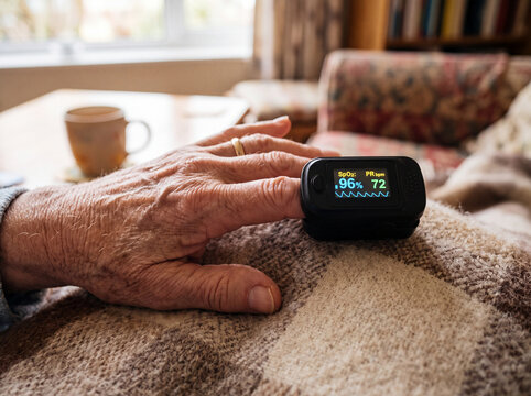 Close-up of an elderly person using a fingertip pulse oximeter at home to monitor blood oxygen saturation and pulse rate, illustrating senior health, self care and medical monitoring.