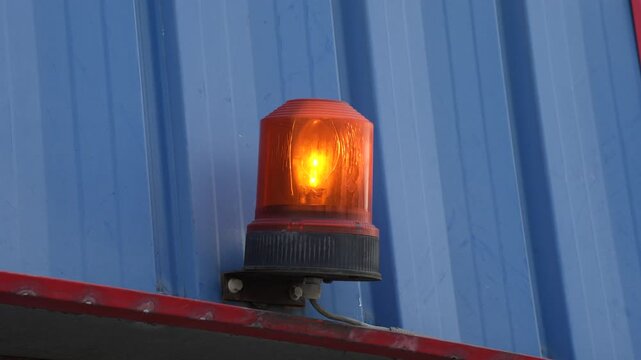 Flashing orange beacon warning light mounted on blue metal corrugated wall representing security system and hazard alert technology