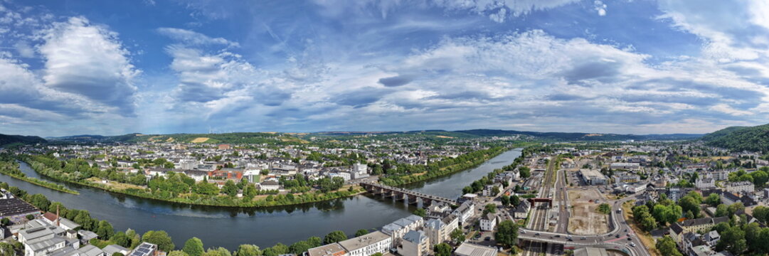Luftbild von Trier mit der antiken R&ouml;merbr&uuml;cke &uuml;ber die Mosel, umgeben von Stadtarchitektur und gr&uuml;nen H&uuml;geln unter bew&ouml;lktem Himmel an einem Sommertag.