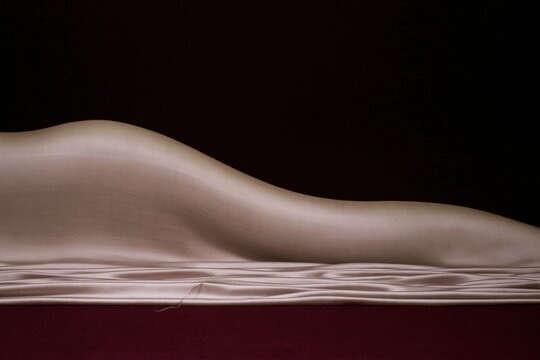Soft rose pink satin fabric drapes in curving folds over a dark crimson backdrop, featuring a luminous silk texture for luxury cosmetics packaging