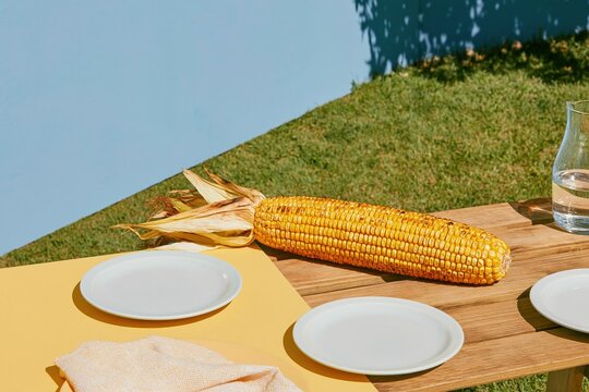 A giant grilled corn cob resting on an outdoor table, featuring charred kernels and warm evening light for food marketing and summer dining concepts