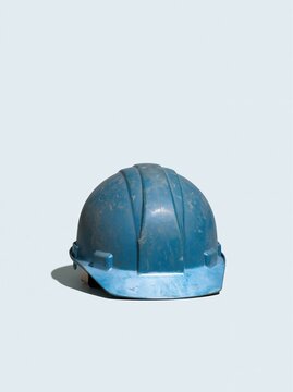 Scuffed blue hard hat resting on a light grey background, featuring a weathered matte texture and worn crown for construction and site safety layouts