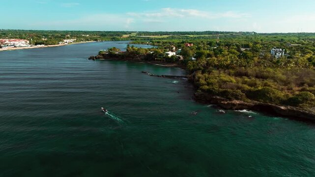 Aerial view of Boca Chavon river mouth with a small boat navigating the blue waters surrounded by lush tropical vegetation in La Romana, La Romana, Dominican Republic.