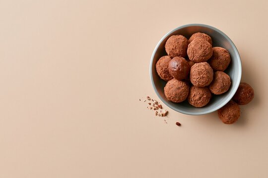 Assorted chocolate truffles with dusted cocoa in a metal bowl on a beige surface with copy space for confectionery packaging and menu design