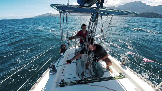 Two men tack and change course of the sailing boat and adjust ropes of the small sailing boat in Brazil