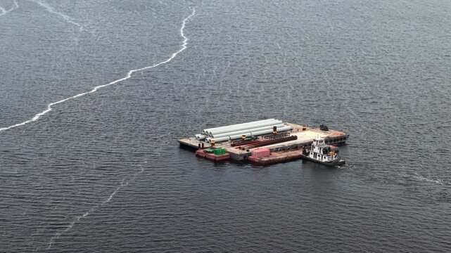 Aerial view of a tugboat pushing a barge loaded with concrete pipes on the St. Johns River near Shands Bridge in St. Augustine, Florida, United States.