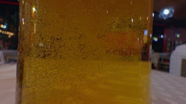 Golden Beer Bubbles Rise Inside a Clear Glass at a Restaurant Table, Showing Refreshment and Dining Ambience Slow motion