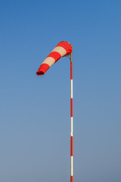 Red and white striped windsock indicates wind direction against a clear blue sky
