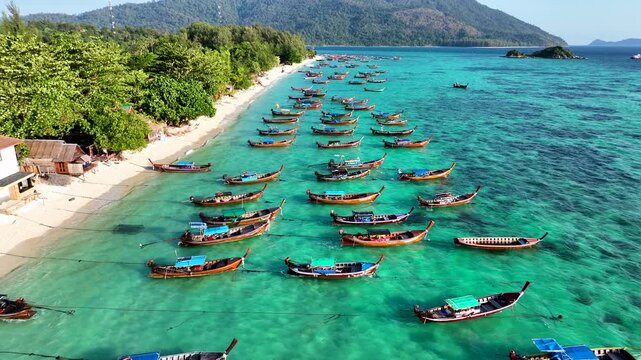 Aerial view of Ko Lipe beach with turquoise water and numerous long-tail boats anchored along the white sand shore in Ko Lipe, Satun, Thailand.