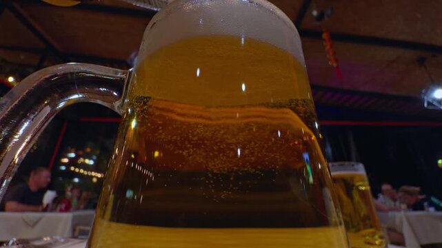 Golden Lager Bubbles in a Glass Mug at a Dining Table, Low Angle Closeup Highlights Foam, Carbonation, and Leisure Lifestyle Slow motion