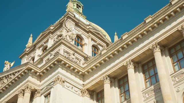 Ornate facade of the National Museum in Prague displays neo-renaissance architecture. Historic landmark features classic columns and golden dome details under a sunny blue sky. Czech travel.
